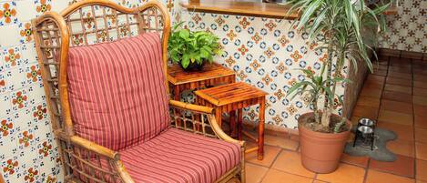 A wicker chair with a striped cushion, a potted plant, and a tiled backsplash with a floral pattern.