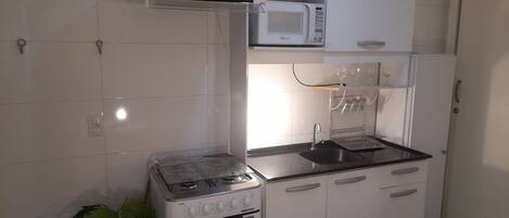 A compact kitchen with white cabinets, a gas stove, a microwave, and a sink.