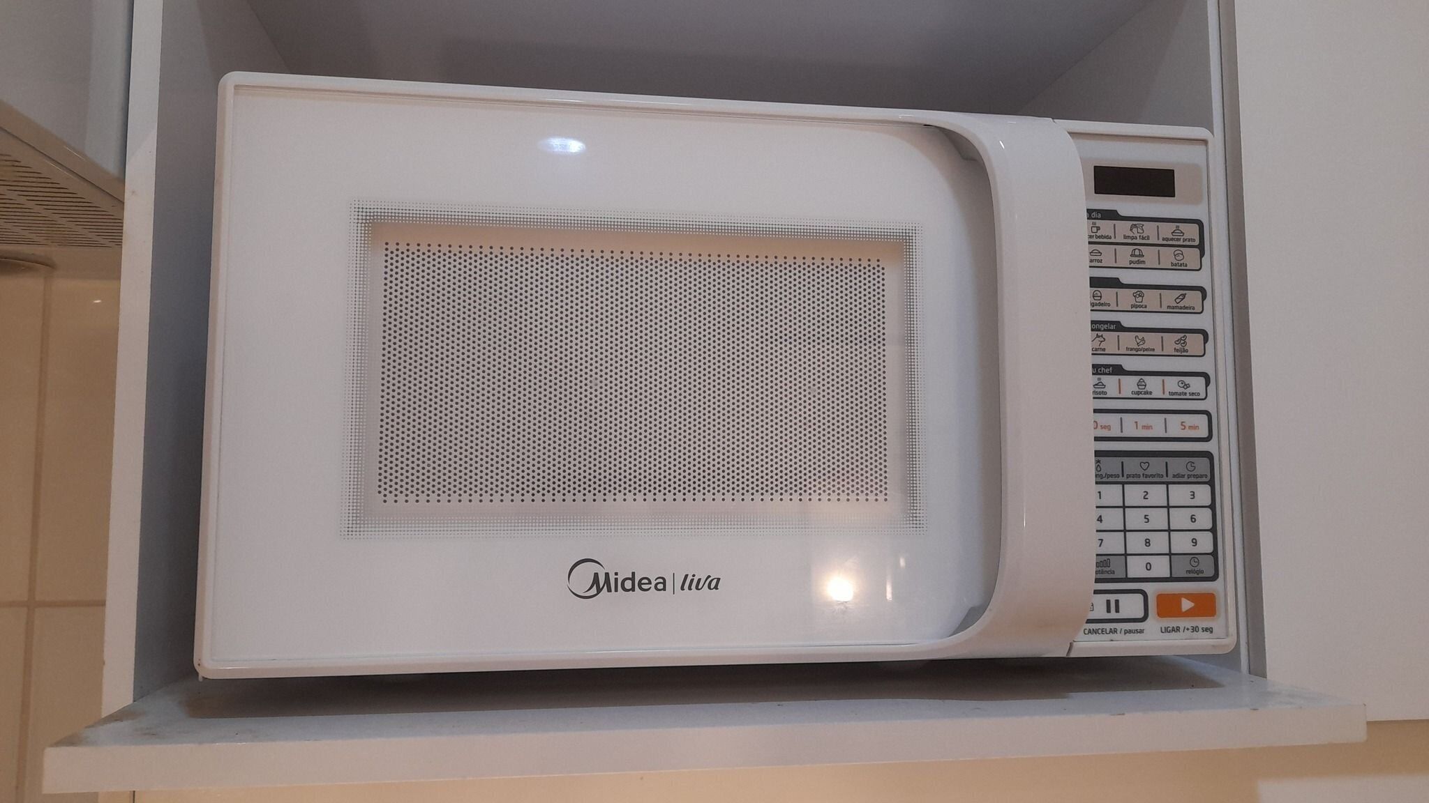 A white Midea microwave oven with a digital control panel, placed on a white shelf.