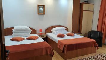 A hotel room with two beds, a nightstand, a lamp, a wardrobe, and a chair.