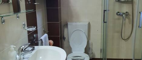 Baño con lavamanos, inodoro y ducha con mampara de vidrio.
