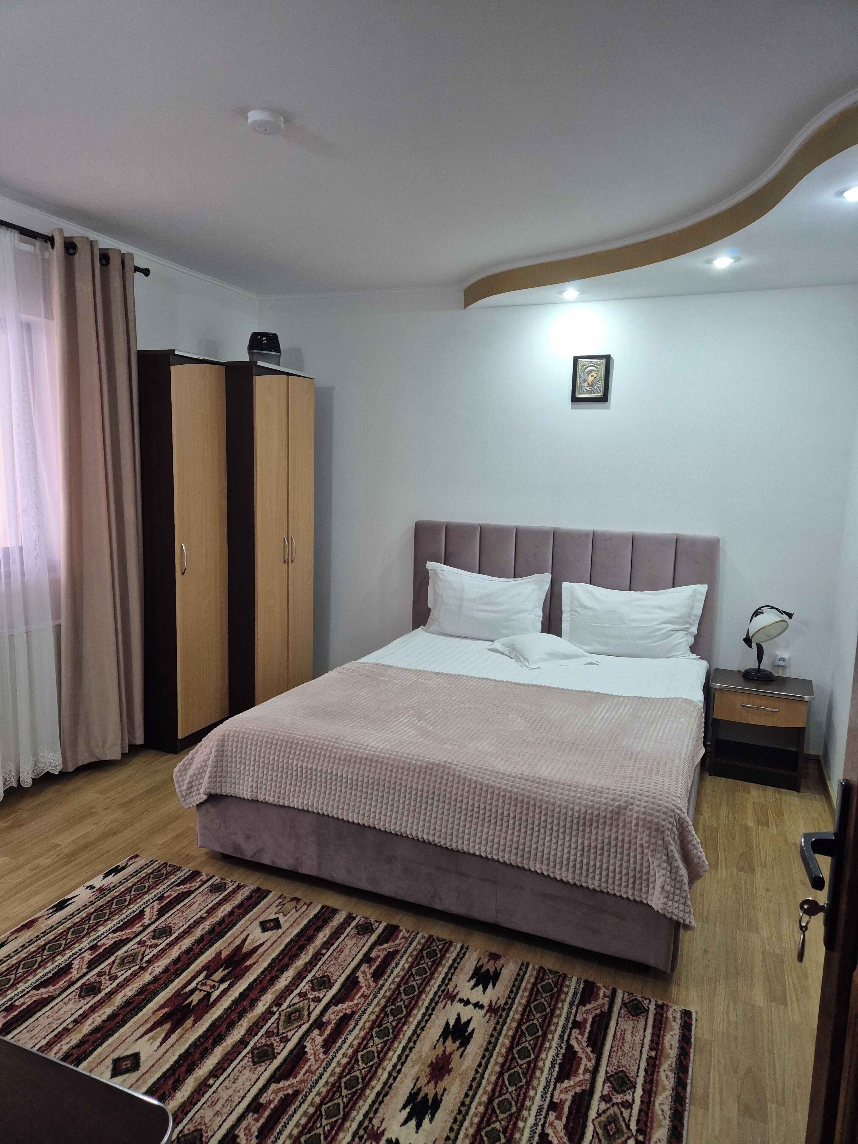 A neatly arranged bedroom with a bed, a bedside table, a wardrobe, and a patterned rug.