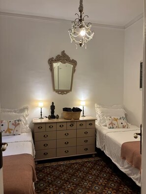 A bedroom with two beds, a dresser, a mirror, and a chandelier.