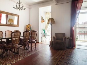 A room with a dining table and chairs, a sofa, a lamp, and a view through an open door.