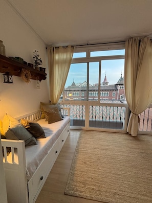 A cozy room with a bed, a small table, and a view of a historic building through large windows.