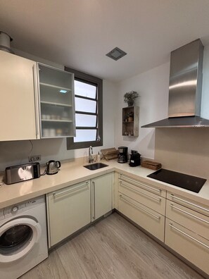 A compact kitchen with a washing machine, a sink, a stove, and a window.