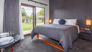 Una habitación de hotel moderna con una cama grande, una zona de comedor con una mesa redonda y vistas al jardín a través de puertas correderas.