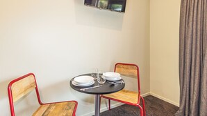 Una habitación pequeña con una mesa, dos sillas, un televisor de pantalla plana en la pared y una ventana con cortinas.