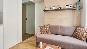 A modern living room with a sofa, a coffee table, and a wooden shelf with decorative items. - Superb Studio Tour Eiffel/champ de Mars (Paris)