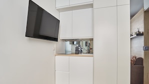 A compact kitchen with white cabinetry, a built-in microwave, and a flat-screen TV mounted on the wall. - Superb Studio Tour Eiffel/champ de Mars (Paris)