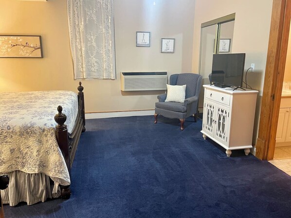 A bedroom with a bed, a chair, a dresser, and a television.
