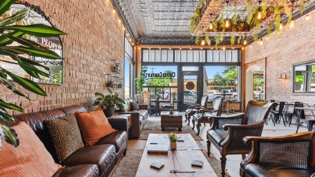 Un rincón interior acogedor con sofás de cuero, mesas de madera y plantas colgantes.