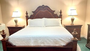 A large wooden bed with a high headboard, flanked by two bedside tables with lamps, in a room with a carpeted floor. - The Eastland Historic Hotel- Imperial Room (Eastland)