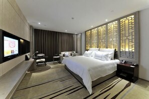 Een moderne hotelkamer met een groot bed, een aan de muur bevestigde televisie, een bureau en een decoratieve scheidingswand.