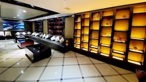 A modern hotel lobby with a black sofa, a coffee table, and a large TV screen. There are shelves with decorative items and a tiled floor. - Yangzhou Convention Center(Mingyue Lake Store) (Yangzhou)