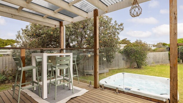 Un espacio al aire libre cubierto con un jacuzzi, terraza de madera y una zona de estar con sillas y una mesa.
