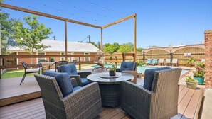 Een overdekt terras buiten met rieten meubilair, een zwembad en een houten terras.