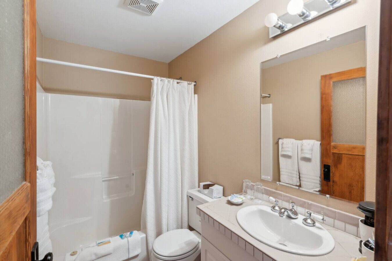 A bathroom with a shower, toilet, sink, and a mirror.