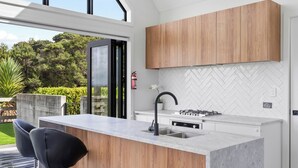 A modern kitchen with a large island, wooden cabinets, and a view of the outdoors. - Estuary Views - Riverhead Holiday House (Auckland)