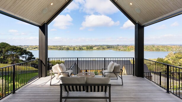 A covered outdoor seating area with a view of a lake and surrounding landscape. - Estuary Views - Riverhead Holiday House (Auckland)