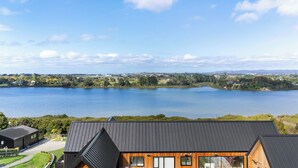 A modern house with a sloped roof, large windows, and a view of a lake. - Estuary Views - Riverhead Holiday House (Auckland)