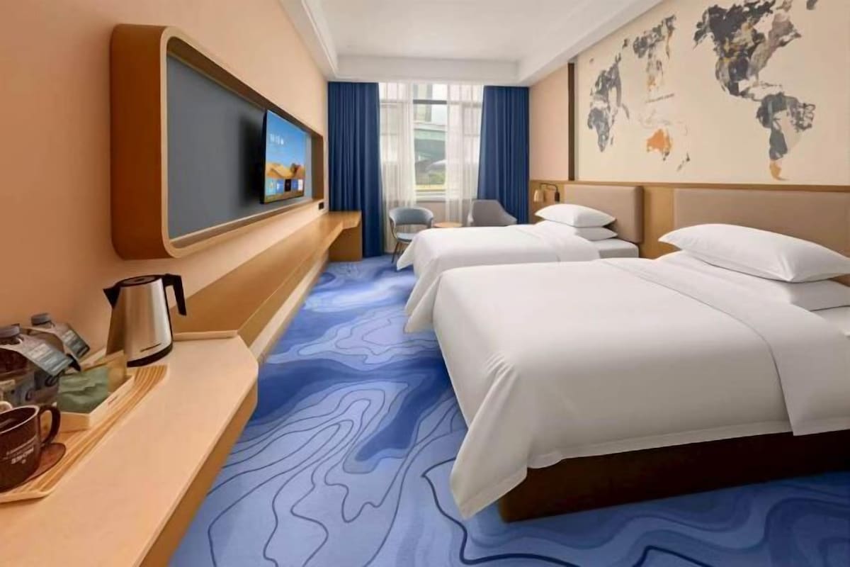 A hotel room with two beds, a television, a desk with a coffee maker, and a world map on the wall.