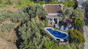 Vista aérea de una propiedad con piscina, zona de patio con sillones de descanso y una casa con techo de tejas.