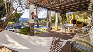 Un patio techado al aire libre con una hamaca, sillas junto a la piscina y una zona de barbacoa.