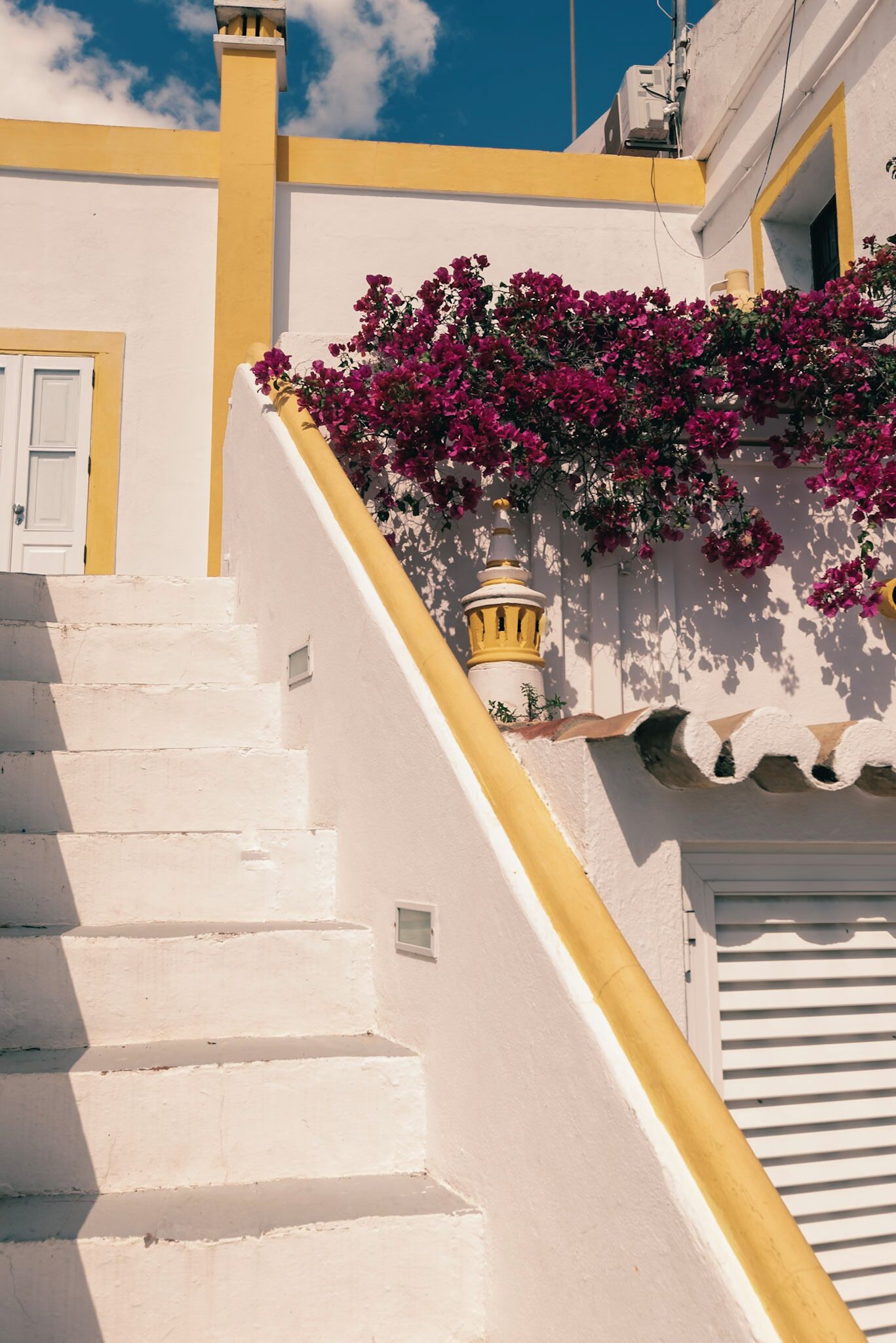 Uma escadaria branca com detalhes amarelos que leva a um edifício com fachada amarela e branca.