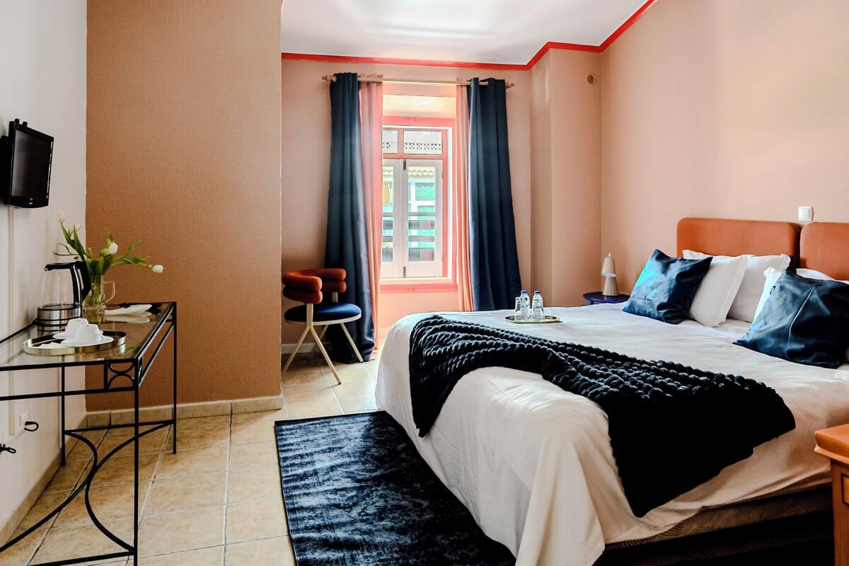 Une chambre d’hôtel avec un lit, une table de chevet et une petite table sur laquelle est posé un vase de fleurs.