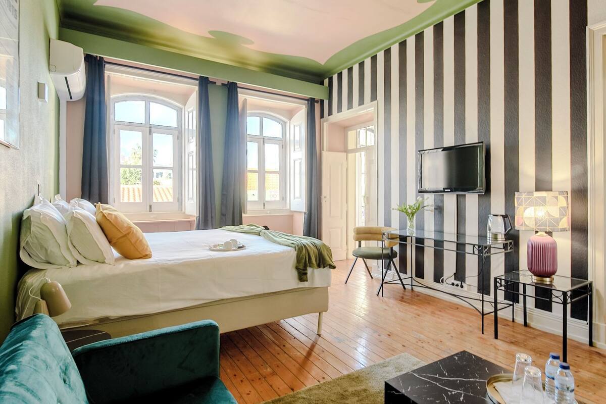 Une chambre d’hôtel avec un lit, une télévision, une petite table avec une lampe et une fenêtre avec des rideaux.