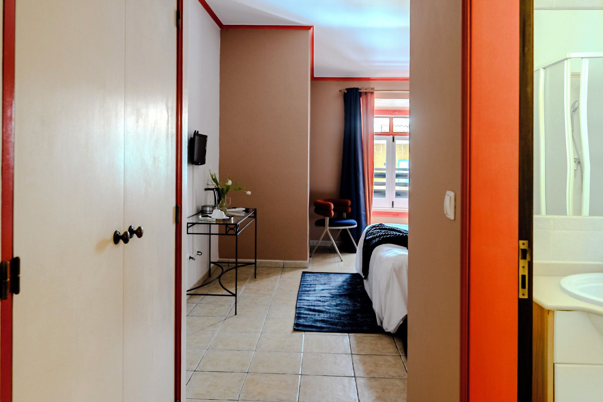 A hotel room with a bed, desk, chair, and a bathroom with a sink and shower.