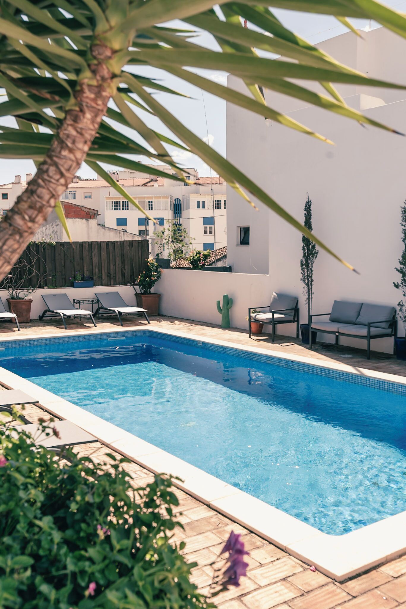 A rectangular swimming pool with clear blue water, surrounded by lounge chairs and potted plants.