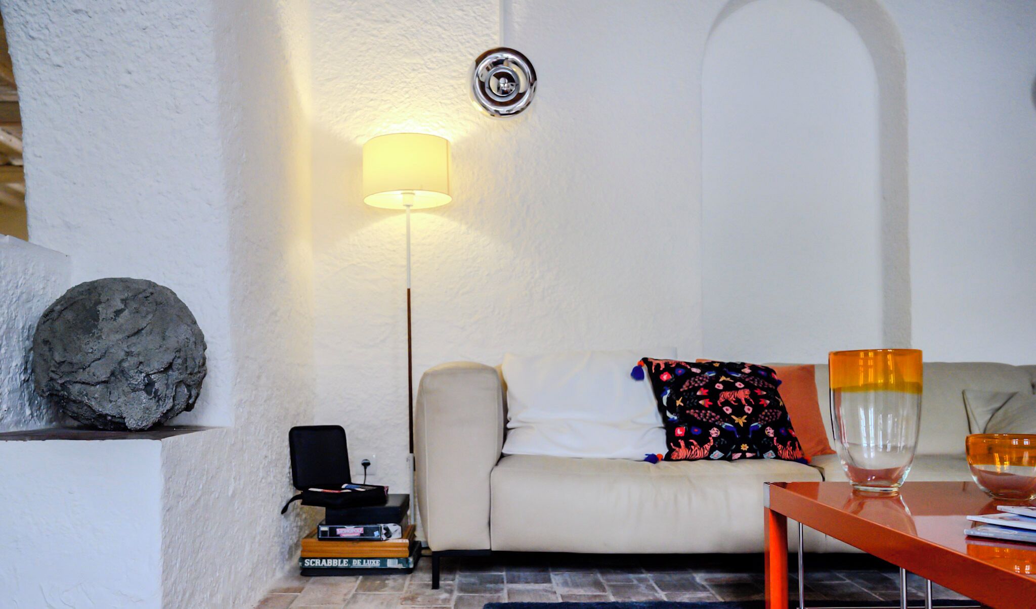 A living room with a white sofa, a lamp, a stone sculpture, a small table with a bowl, and a stack of books.