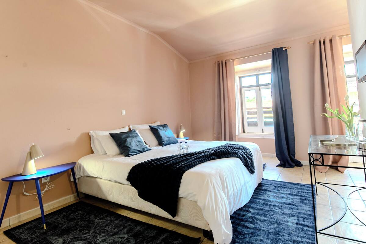 Une chambre à coucher avec un lit, une table de chevet, une lampe et une fenêtre avec des rideaux.