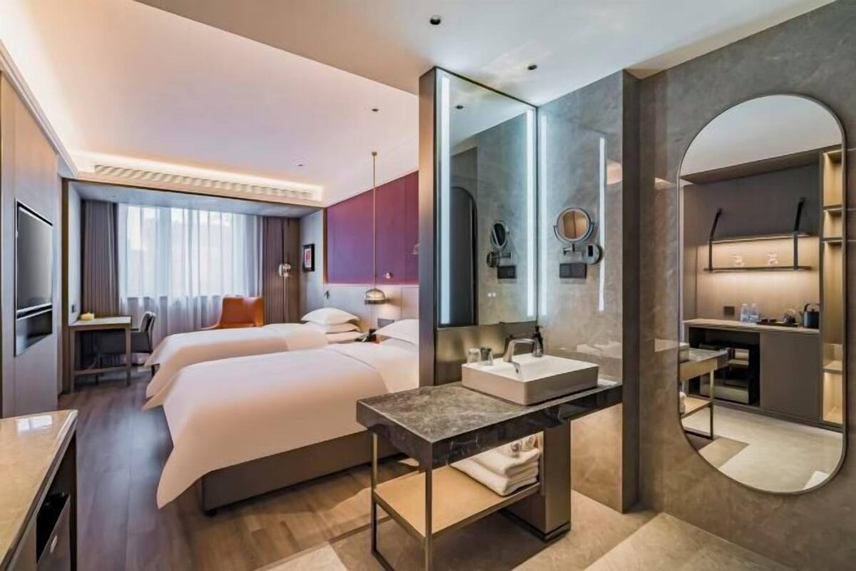Een moderne hotelkamer met twee bedden, een grote spiegel, een wastafel met marmeren blad en een bureau.