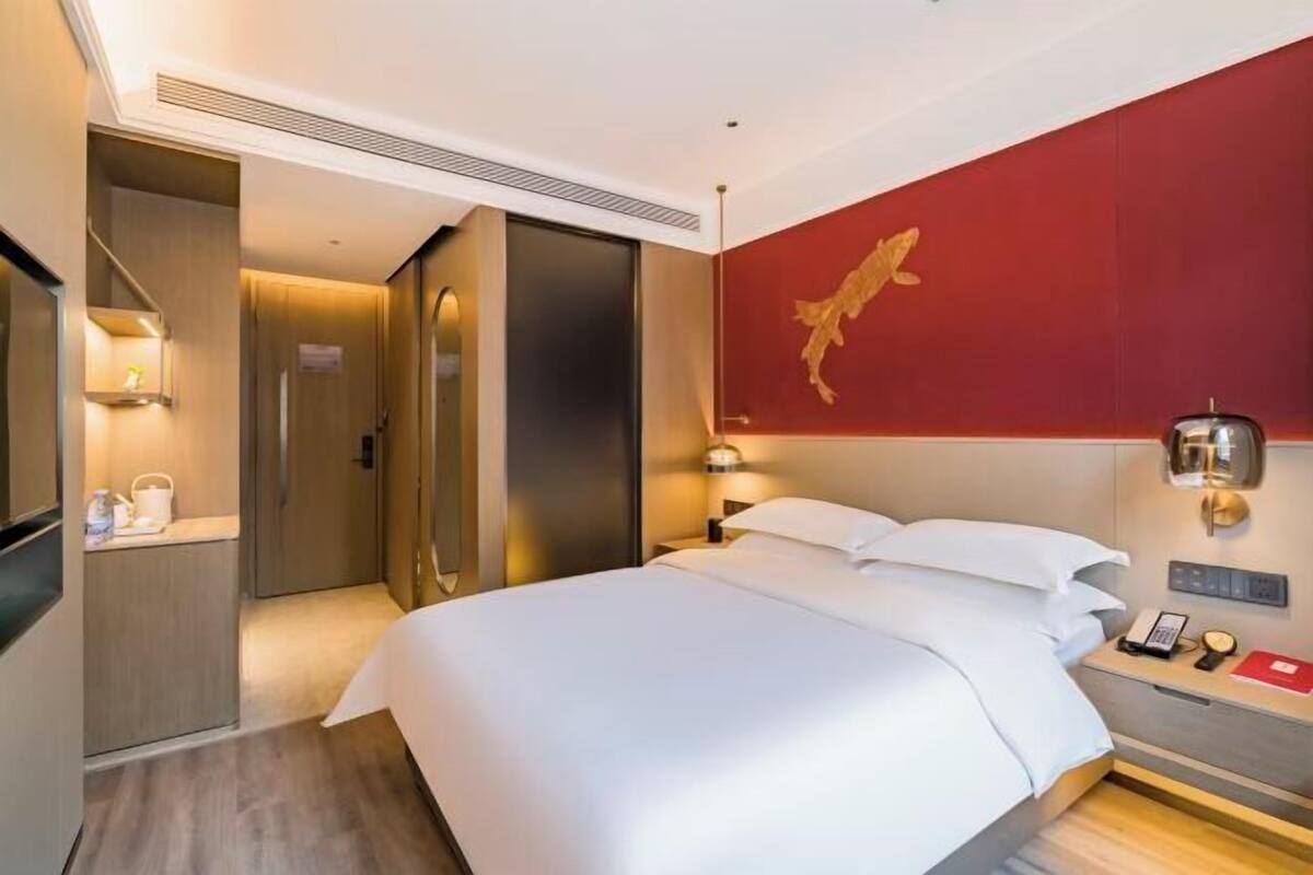Een hotelkamer met een bed, nachtkastje, lamp en een rode accentmuur.