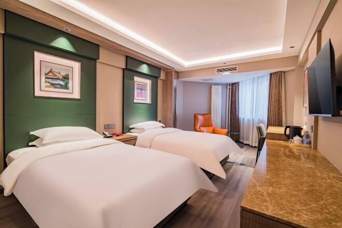 Een hotelkamer met twee bedden, een bureau, een stoel, een televisie en foto's in lijsten aan de muur.