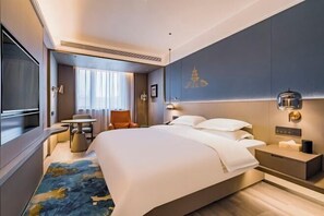 A modern hotel room with a large bed, a desk, a chair, and a view of the city.