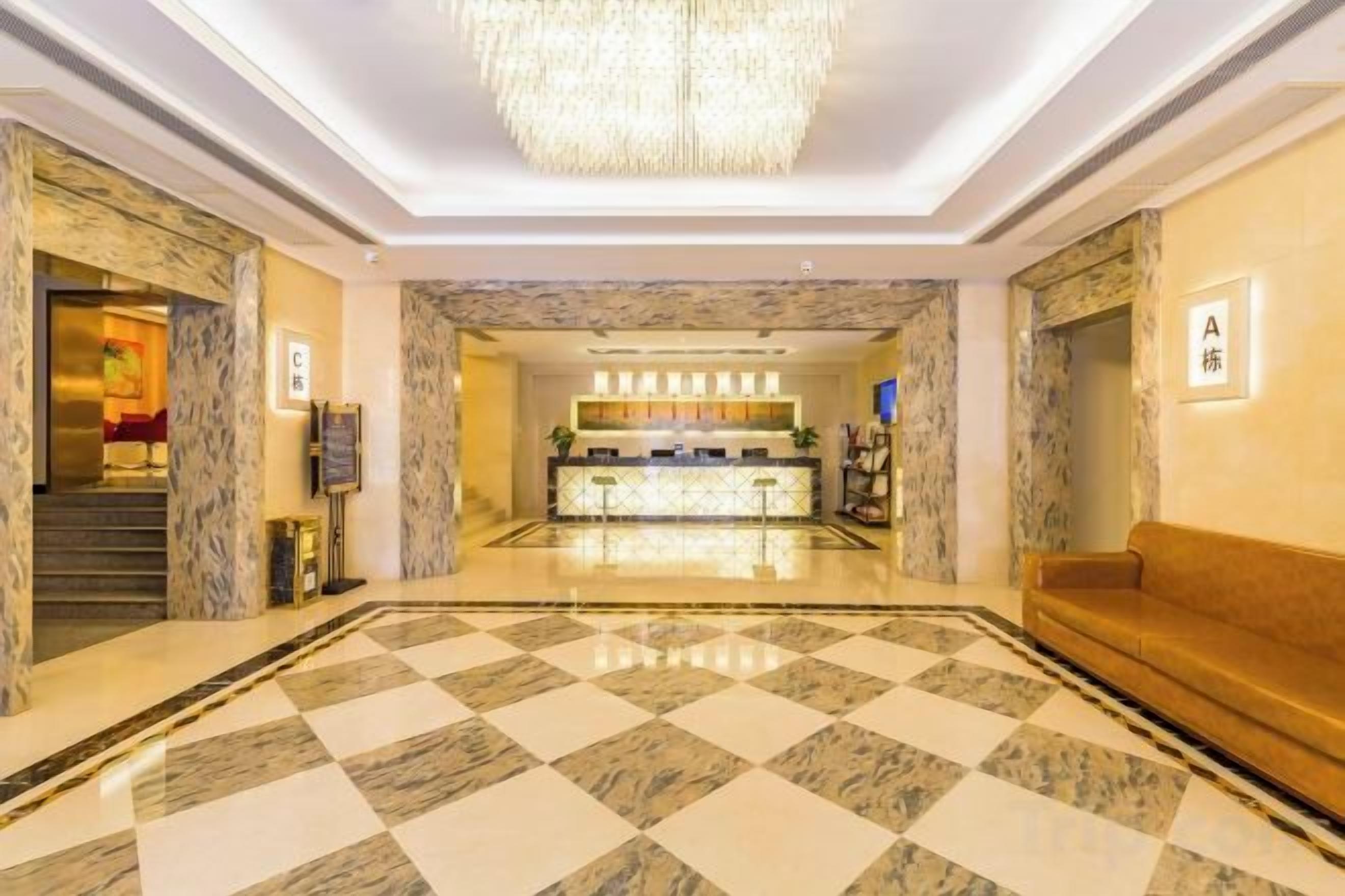 A hotel lobby with a checkered floor, a reception desk, a chandelier, and a sofa.