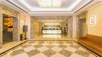 A hotel lobby with a checkered floor, a reception desk, a chandelier, and a sofa.