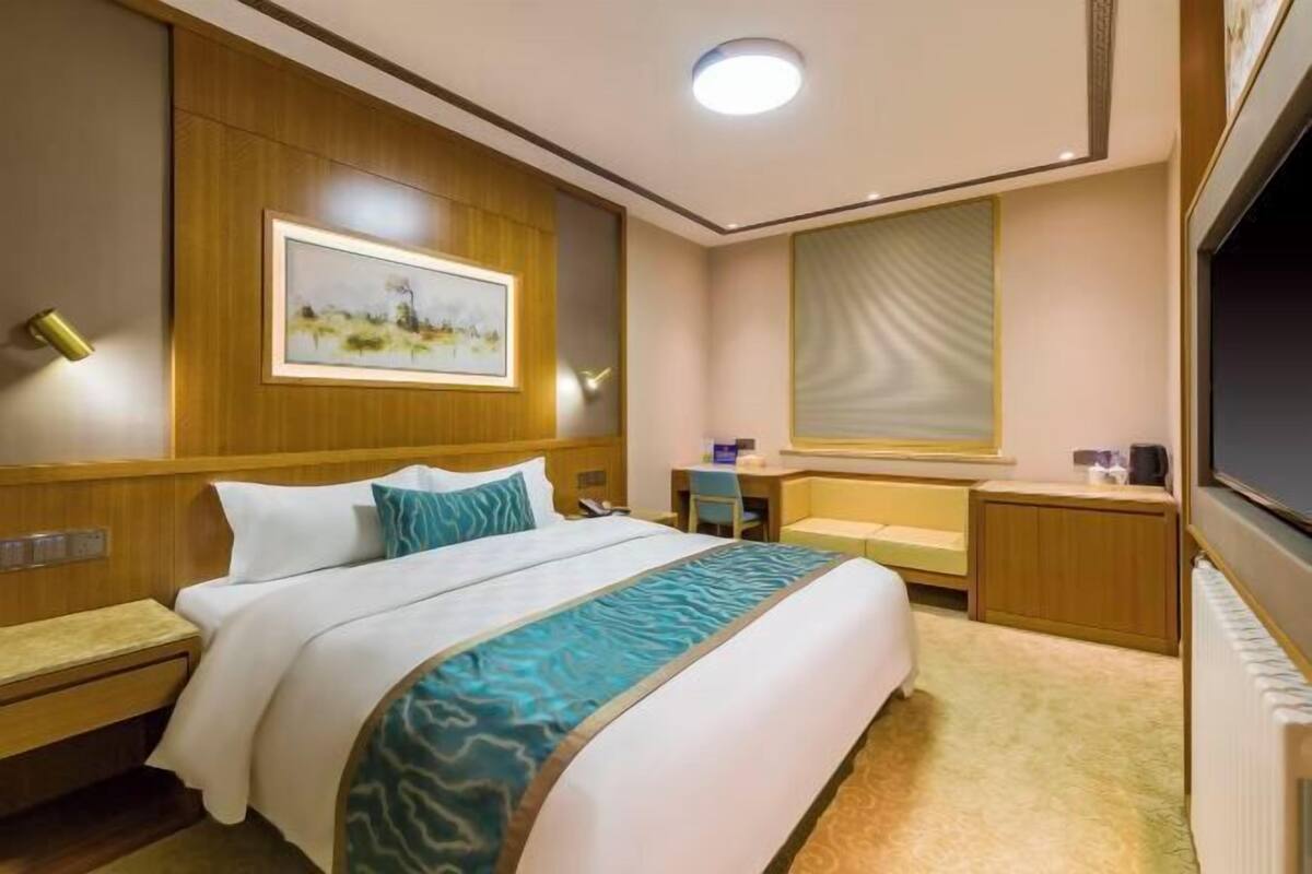 Een hotelkamer met een bed, nachtkastjes, een bureau, een stoel, een televisie en een schilderij aan de muur.