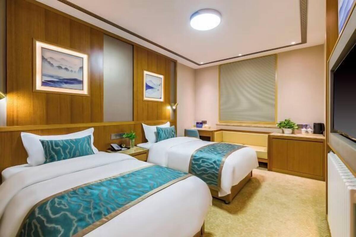 Een hotelkamer met twee bedden, een bureau, een spiegel en een raam met zonwering.