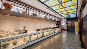 A spacious corridor with a high ceiling and skylight, leading to a reception area with a counter and seating.