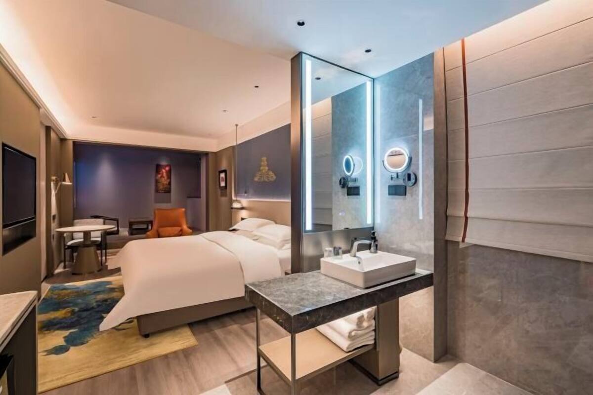 Een moderne hotelkamer met een bed, nachtkastje en een grote spiegel.