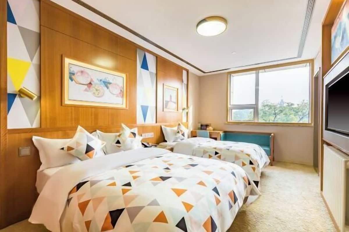 Een hotelkamer met twee bedden, houten lambrisering, ingelijste kunst en een groot raam, plus een televisie.