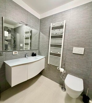 Een moderne badkamer met een witte wastafel, een grote spiegel, een handdoekrek en een toilet.