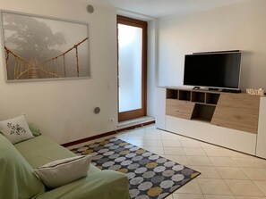 A living room with a green sofa, a TV on a wooden stand, a patterned rug, and a painting of a bridge.