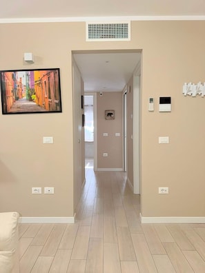 A hallway with beige walls, a tiled floor, a picture of a colorful street, a vent, and a thermostat.