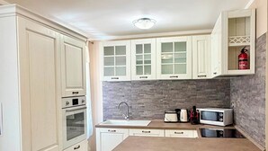 A kitchen with white cabinetry, a tiled backsplash, a double oven, a sink, and two bar stools. - Casa Magenta Apartment 2 (Valeggio sul Mincio)